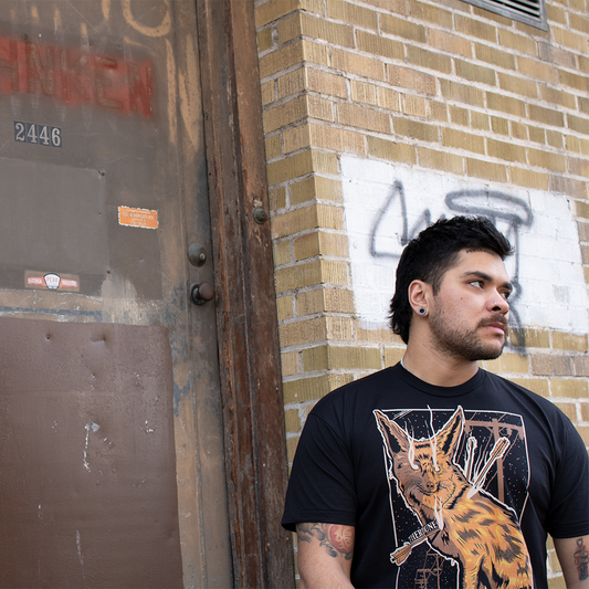 Black shirt with a graphic of a fox impaled with arrows. Worn by a model in front of a brick wall.