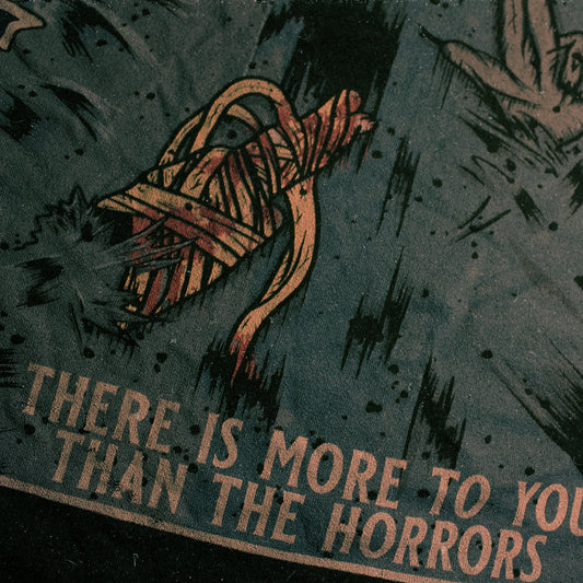 Black shirt with a graphic of a raccoon with an injured, bandaged arm. Text that says "There is more to you than the horrors".