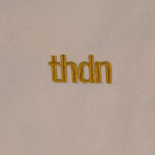 Close-up of a dust colored fitted fleece pant laid flat. A gold "thdn" logo is embroidered on the fabric.