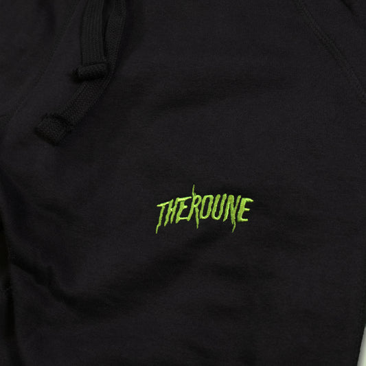 Close-up of a black joggers featuring a bright lime green embroidered 'Therdune' logo, with black drawstrings visible at the top.