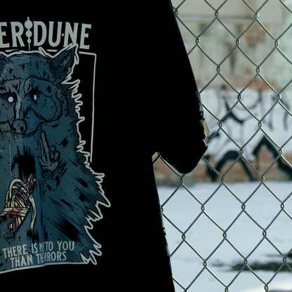 Black shirt with a graphic of a raccoon with an injured, bandaged arm. Text that says "There is more to you than the horrors" hanging from chainlink fence. 