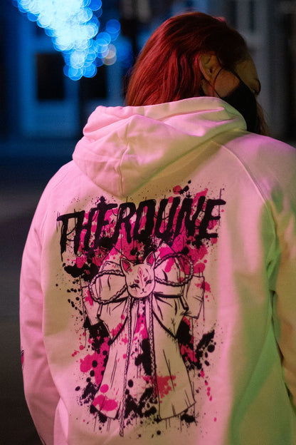 Back of a white color hoodie with a graphic of a bow with pink and black paint splatter and a Therdune logo. Worn by a model in an urban environment.