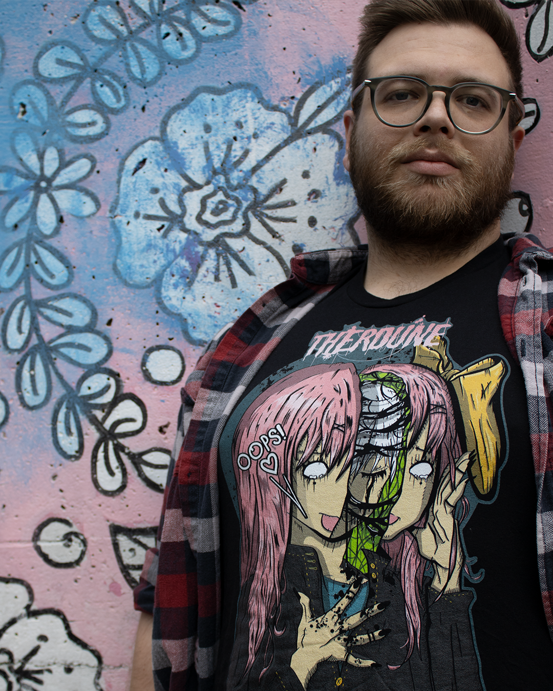 Black shirt with an anime face splitting in half with a crying person inside. Worn by a model with a floral background.