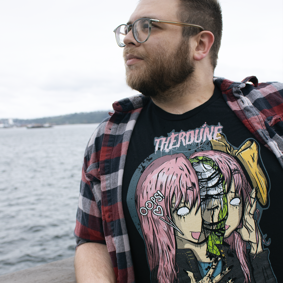 Black shirt with an anime face splitting in half with a crying person inside. Worn by a model looking out at the ocean.