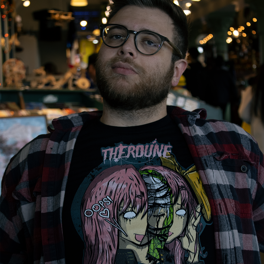 Black shirt with an anime face splitting in half with a crying person inside. Worn by a model in a cafe.