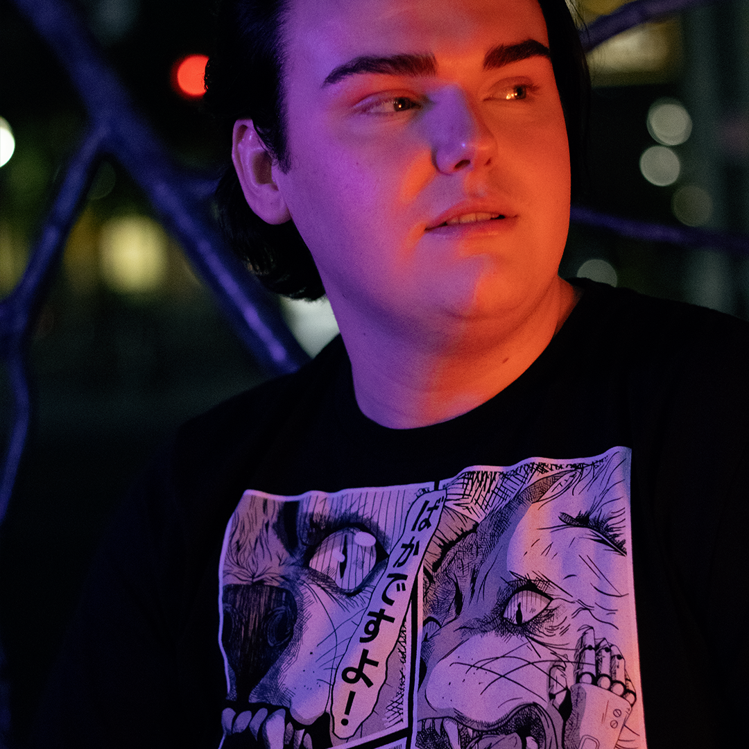 Black shirt with with 4 panel manga style illustration with japanese text and Therdune logo, worn by model, in urban setting.