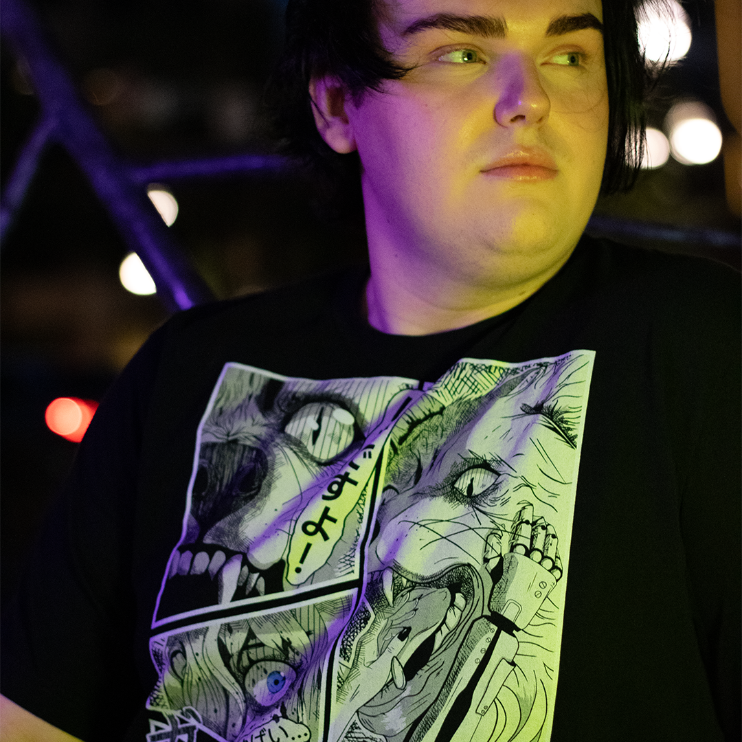 Black shirt with with 4 panel manga style illustration with japanese text and Therdune logo, worn by model, sitting on bench.