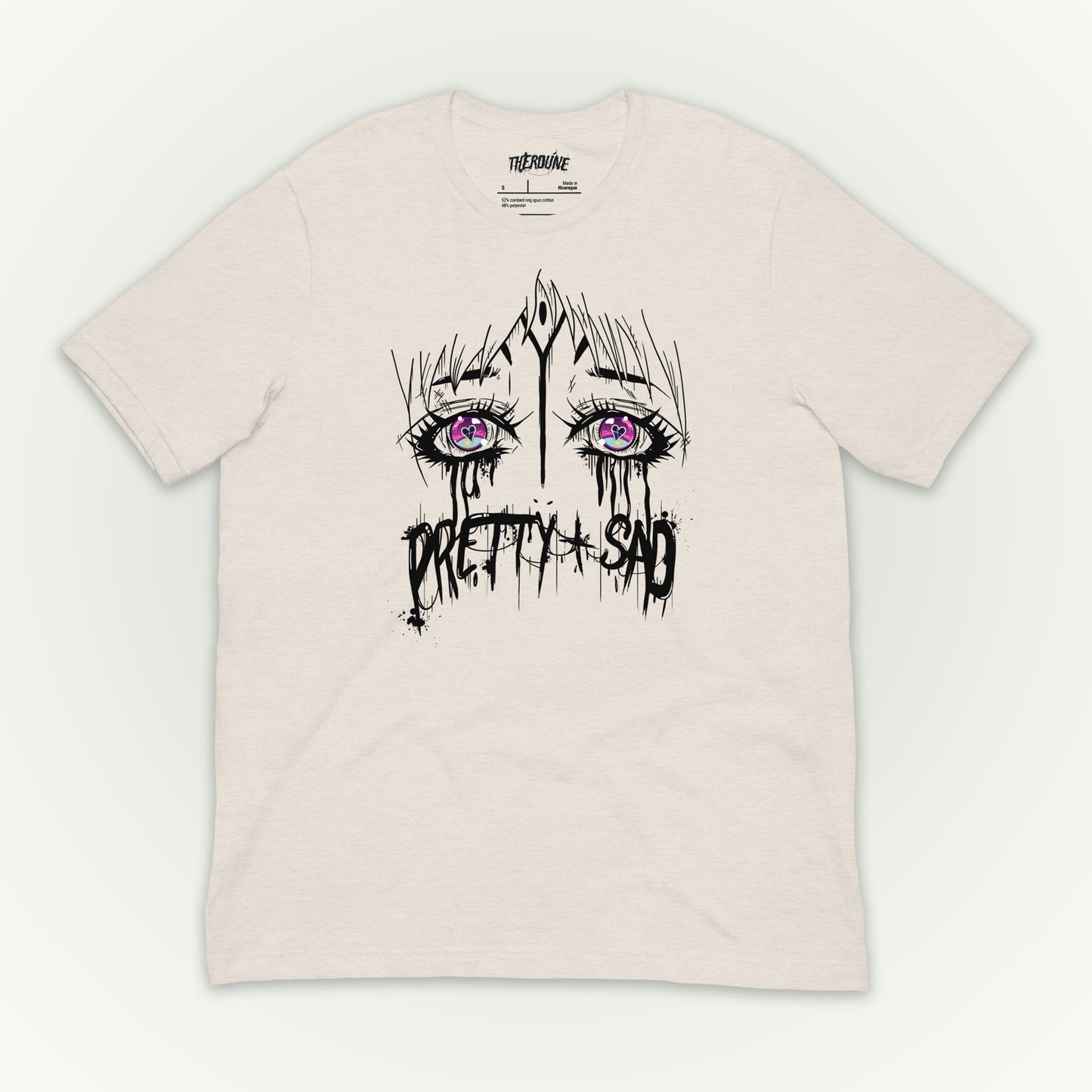 Cream color shirt with a graphic print of stylized eyes and the text 'Pretty & Sad' on the front. flat lay on white background.