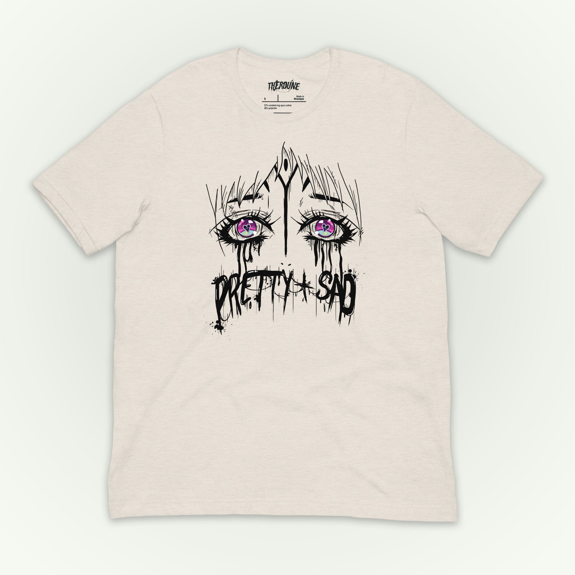 Cream color shirt with a graphic print of stylized eyes and the text 'Pretty & Sad' on the front. flat lay on white background.