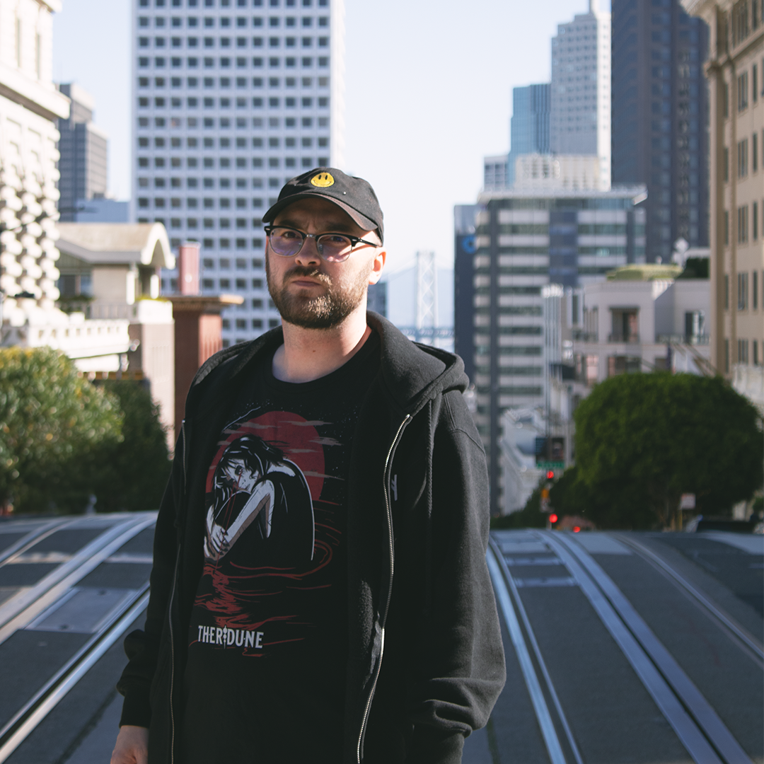Black shirt with a graphic of a woman crying in knee high water with a red moon in the background. Worn by a model in an urban city.