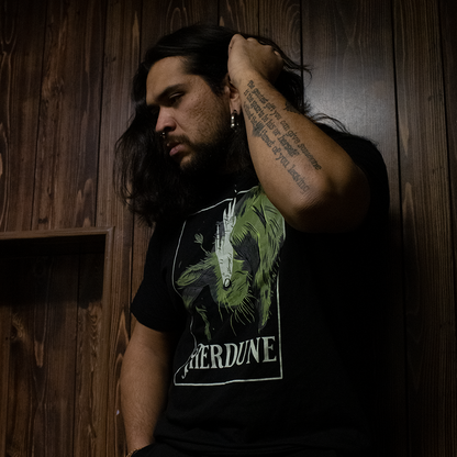 Black shirt with graphic of a falling rabbit, smokey tears coming out from the rabbit's eye. "Therdune" logo framed below, worn by model, standing against a wood panel wall.