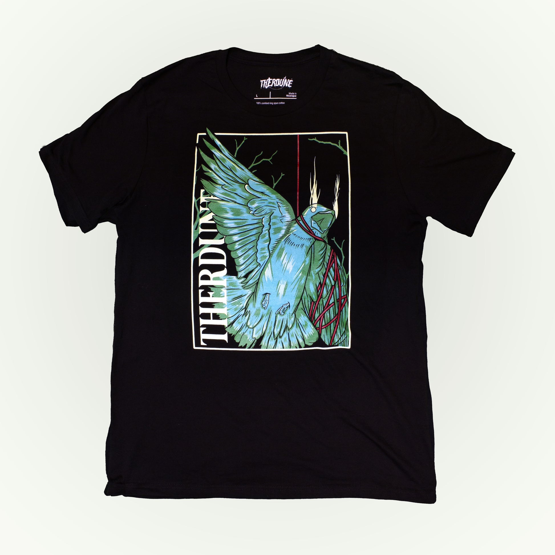 Black shirt with stylized graphic of a green bird, one wing and neck is wrapped up with a red piece of string. "Therdune" logo written on left side vertically. Flat lay on white background.