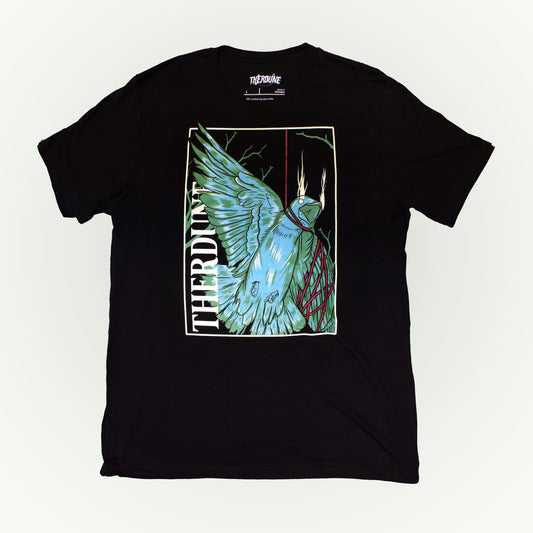 Black shirt with stylized graphic of a green bird, one wing and neck is wrapped up with a red piece of string. "Therdune" logo written on left side vertically. Flat lay on white background.