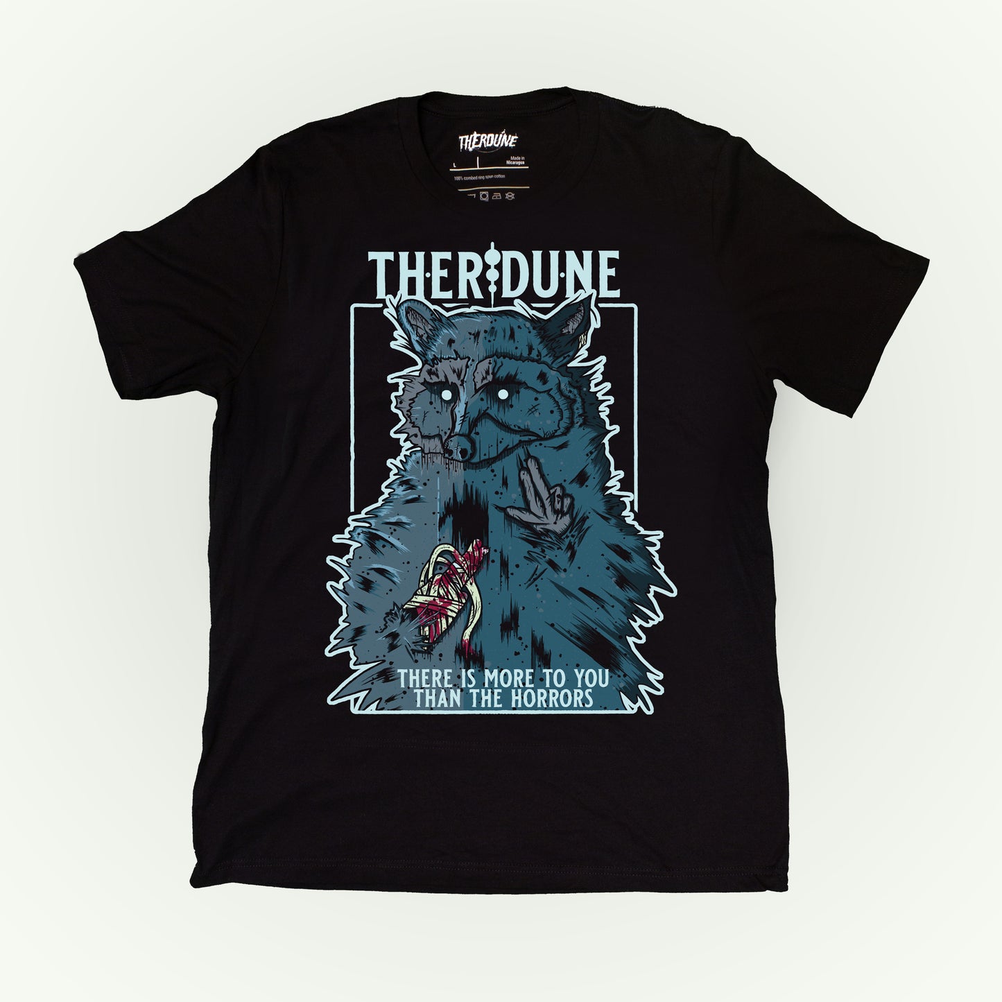 Black shirt with a graphic of a raccoon with an injured, bandaged arm. Text that says "There is more to you than the horrors" flat lay on white background.