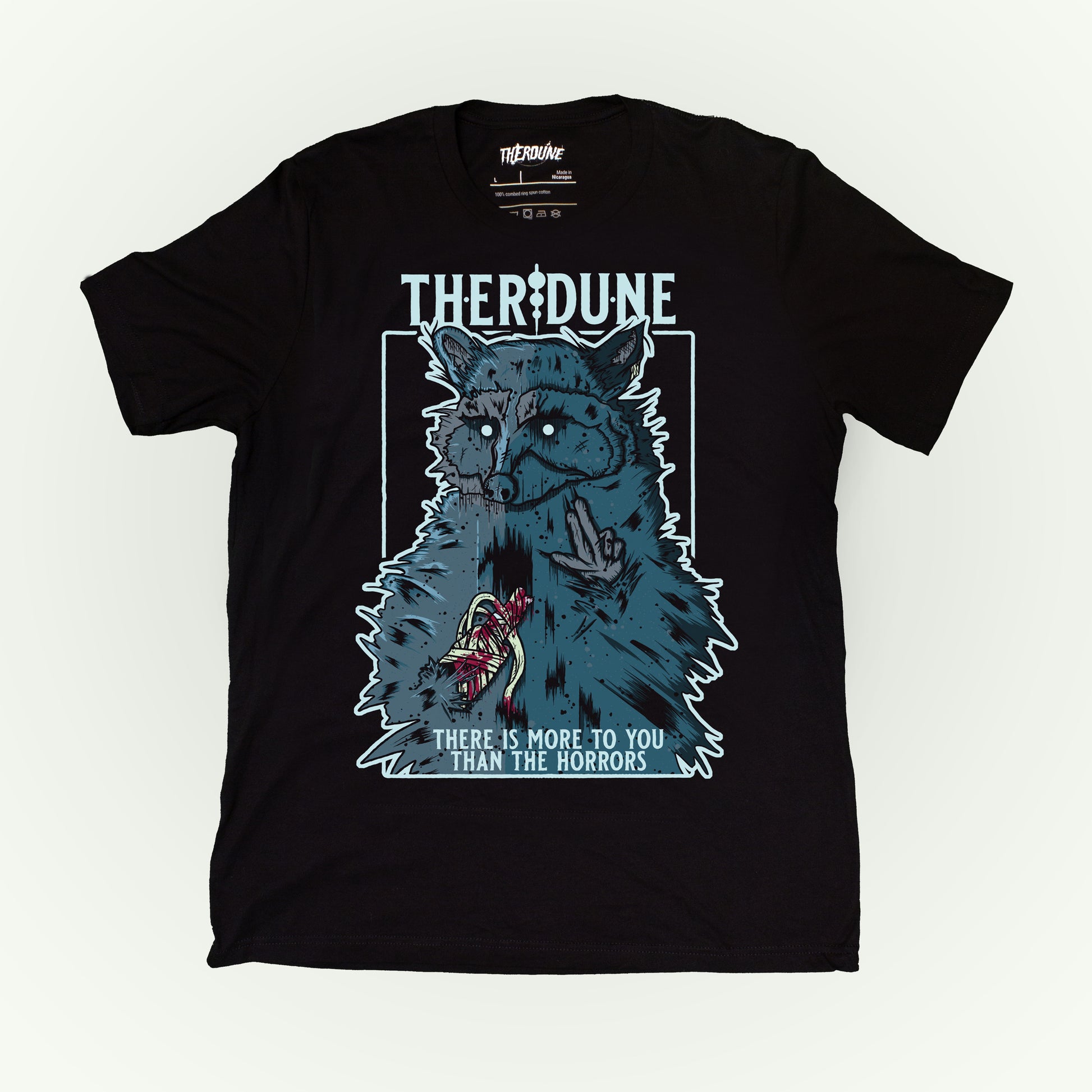 Black shirt with a graphic of a raccoon with an injured, bandaged arm. Text that says "There is more to you than the horrors" flat lay on white background.