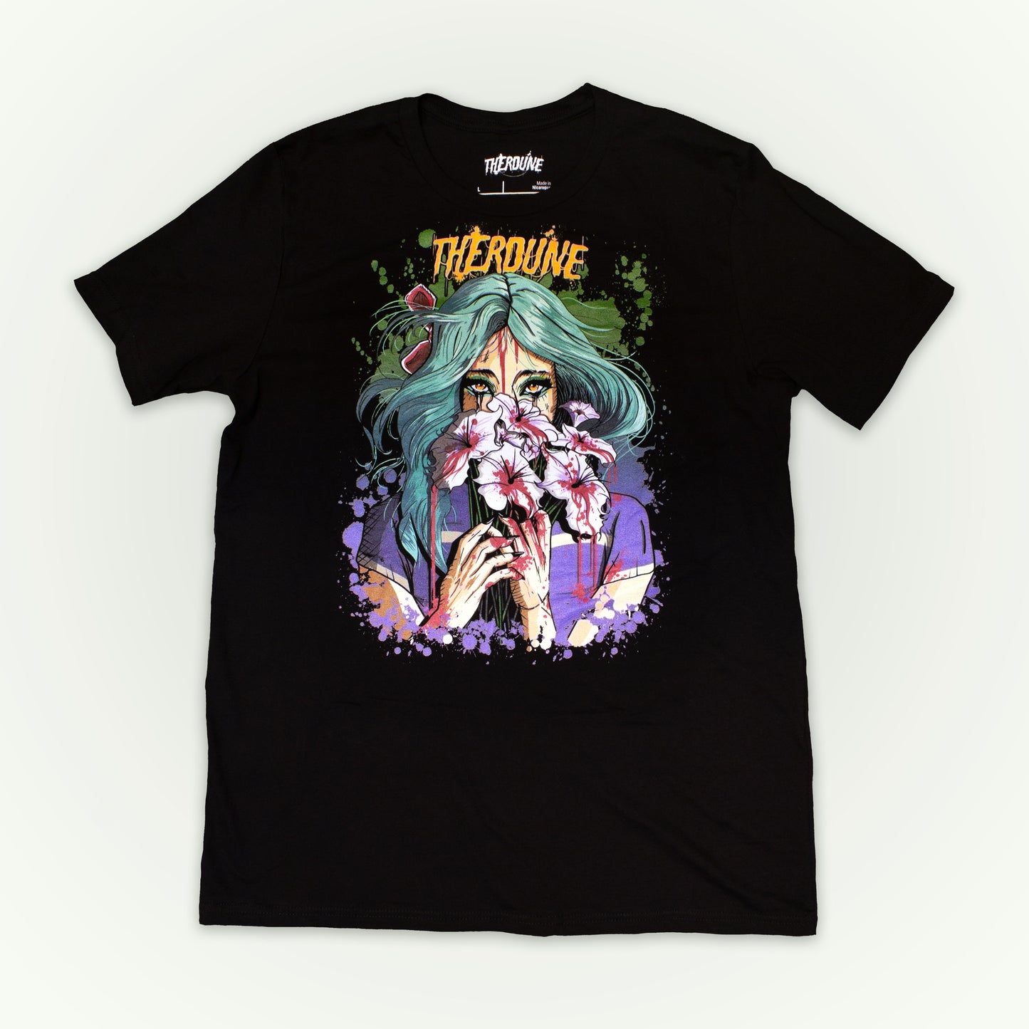 Black shirt with a stylized illustration of a person with teal hair and colorful makeup. Flat lay on white background.