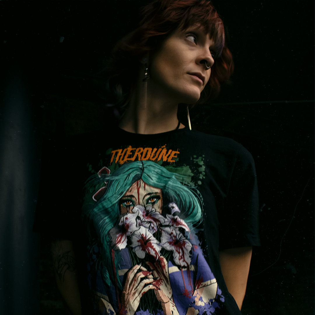 Black shirt with a stylized illustration of a person with teal hair and colorful makeup, worn by a model on a black background.