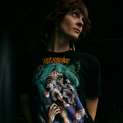 Black shirt with a stylized illustration of a person with teal hair and colorful makeup, worn by a model on a black background.