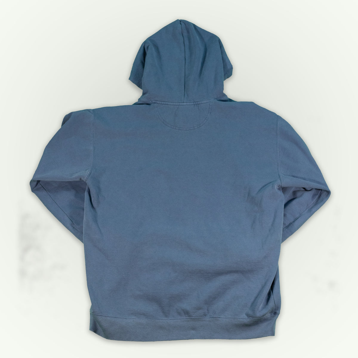 The back of a blue jean colored hooded sweatshirt, displayed flat against a light off-white background.