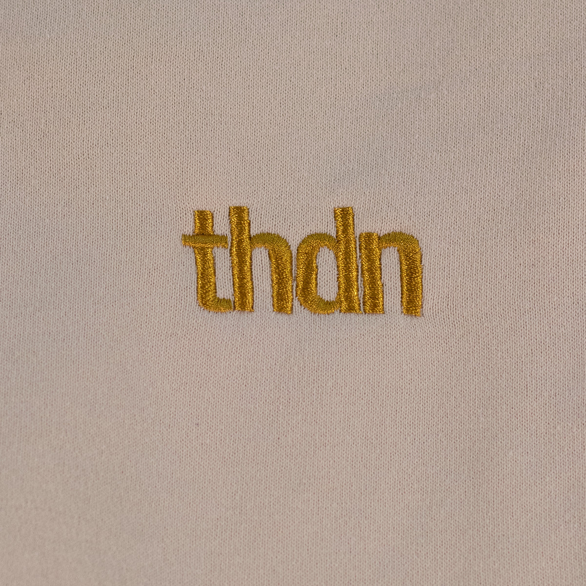 Close-up of a dust colored fitted fleece pant laid flat. A gold "thdn" logo is embroidered on the fabric.