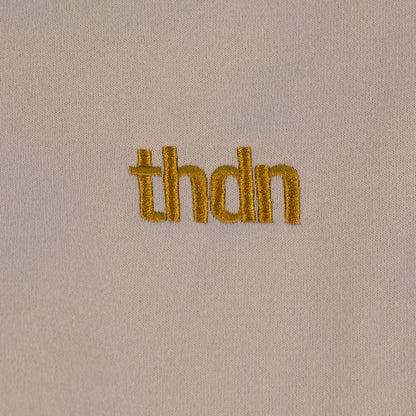 Close-up of a dust colored fitted fleece pant laid flat. A gold "thdn" logo is embroidered on the fabric.