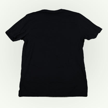 The back of a plain black short-sleeve crewneck t-shirt shown from the back, laid flat against a light off-white background.