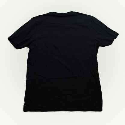The back of a plain black short-sleeve crewneck t-shirt shown from the back, laid flat against a light off-white background.