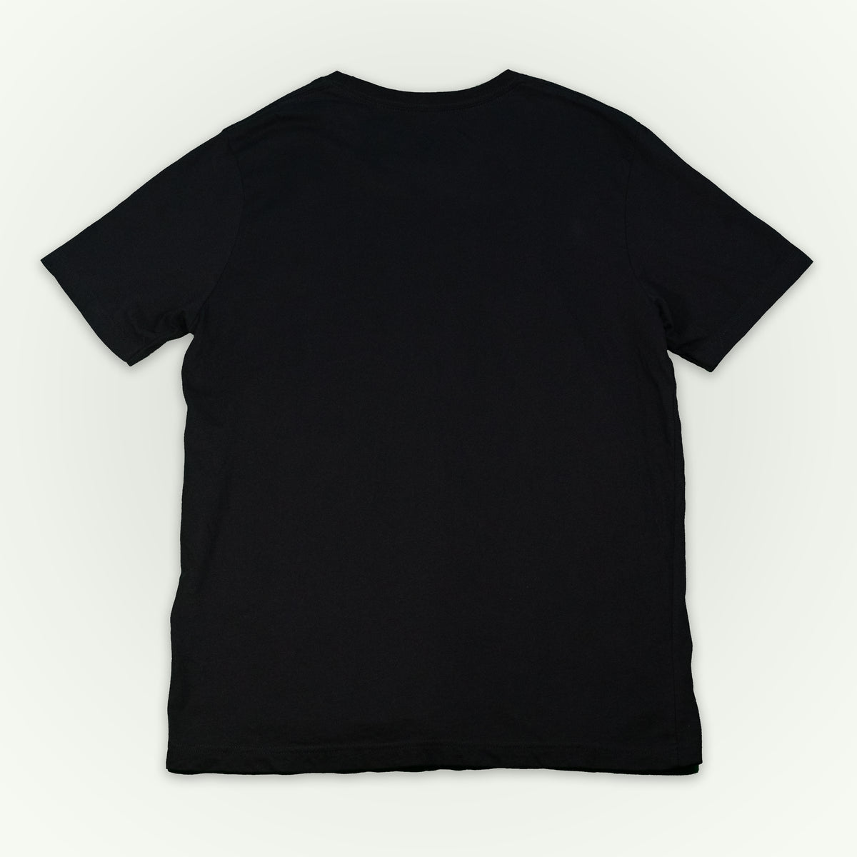 The back of a black short-sleeve crewneck t-shirt laid flat against a light off-white background. 