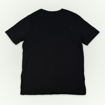 The back of a black short-sleeve crewneck t-shirt laid flat against a light off-white background. 