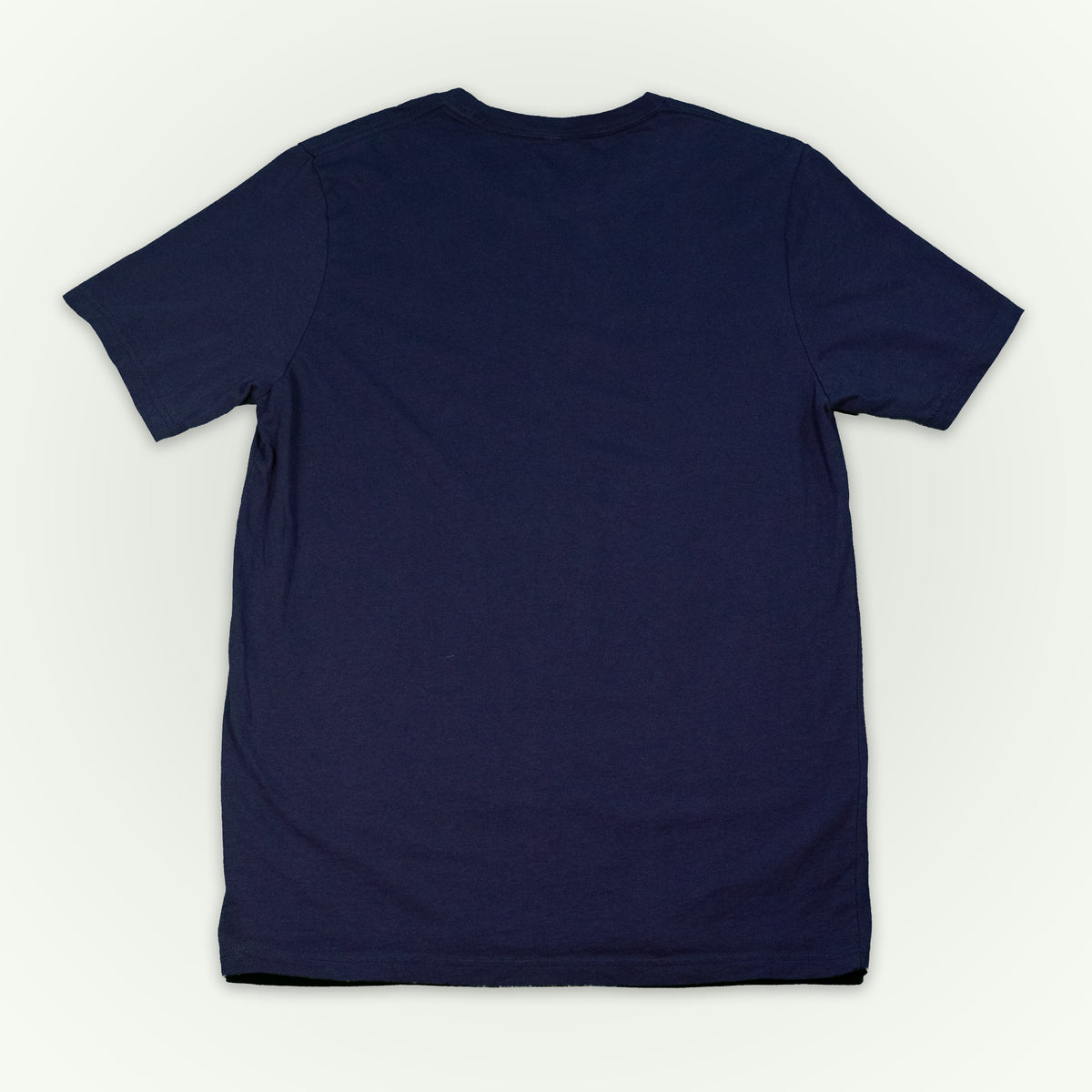 The back of a navy short-sleeve crewneck t-shirt laid flat against a light off-white background. 