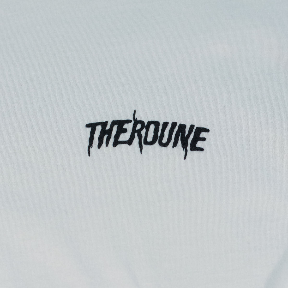 Close-up of a white short-sleeve crewneck t-shirt laid flat. A black Therdune logo is printed on fabric.