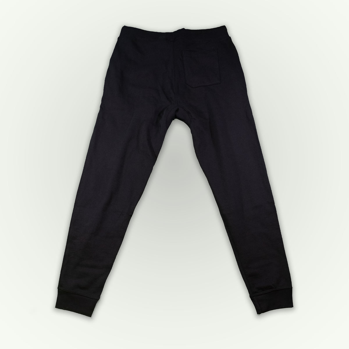 Black sweatpants shown from the back, featuring a single back pocket and ribbed cuffs, laid flat on a light white background.