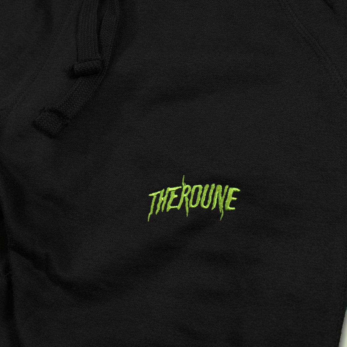 Close-up of a black joggers featuring a bright lime green embroidered 'Therdune' logo, with black drawstrings visible at the top.