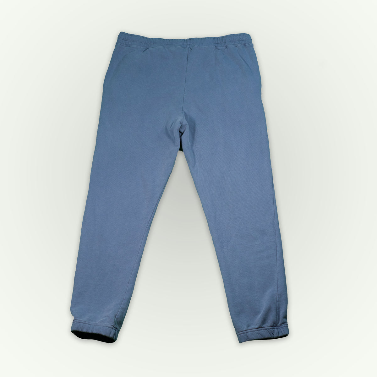 The back of blue jean colored fitted sweatpants, displayed flat against a light off-white background.