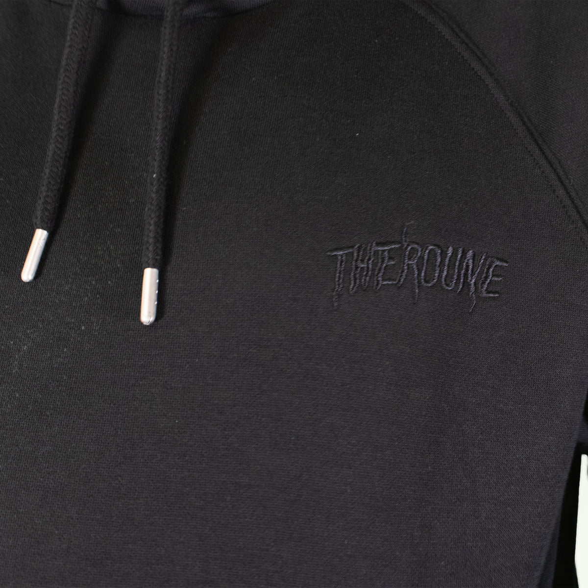 Close-up of a black pullover hoodie with black drawstrings and a tonal black embroidered logo reading 'Therdune' on the chest.