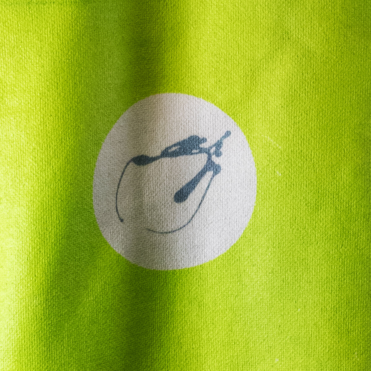 Close-up of a bright lime green fabric surface with a circular white patch containing a dark blue abstract slug-like logo.