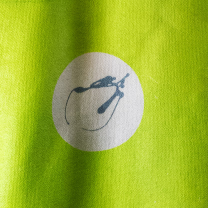 Close-up of a bright lime green fabric surface with a circular white patch containing a dark blue abstract slug-like logo.