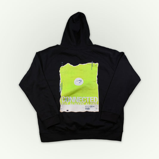 A black pullover hoodie laid flat against a light off-white background, featuring a large graphic print on the front in neon yellow-green and beige with the text 'CONNECTED, BUT ALL ALONE'.